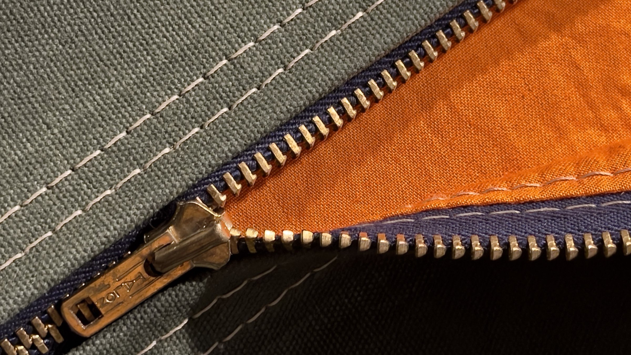 Vintage Talon brass zipper on waxed OD canvas. Behind the teeth, the orange face of a Combat Identification Panel lining.
